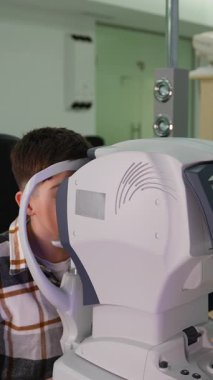 Bir göz hekiminde modern bir otorefraktör kullanan genç adam görme testi. Görme düzeltmesi için göz muayenesi yapılan bir hasta