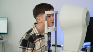 Göz hekimliği sınavına giren küçük bir çocuk. Görme kontrolü ve tanılama için modern bir otomatik fraktör arayan bir hasta.
