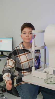 Göz muayenesinden geçen genç bir çocuk göz hekimliği kliniğinde. Kameraya bakıp işaret eden mutlu bir hasta.