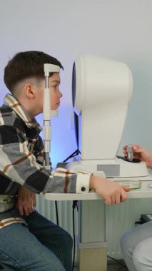 Genç bir çocuk modern bir göz hastalıkları kliniğinde göz muayenesi oluyor. Teşhis için temas olmayan tonometre kullanan profesyonel optometrist
