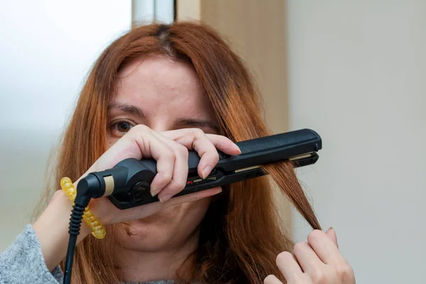 Woman using a hair straightener to straighten her hair