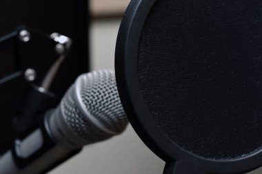 Bir pop filtresiyle korunan bir mikrofona yaklaş.