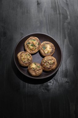 Şampiyon atıştırmalığı: fırında peynir ve şapkalı yeşiller. Ev yapımı yemekler, çiçek çemberi mantarları tahta bir masada siyah bir tabakta.