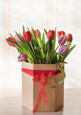 Güneşli bir günde, bir vazoda kırmızı ve mor laleler. Sevilen birinin hediyesi olan kurdeleli bir vazo.