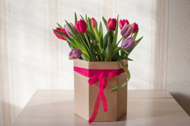 Güneşli bir günde, bir vazoda kırmızı ve mor laleler. Sevilen birinin hediyesi olan kurdeleli bir vazo.