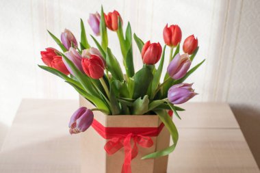 Güneşli bir günde, bir vazoda kırmızı ve mor laleler. Sevilen birinin hediyesi olan kurdeleli bir vazo.