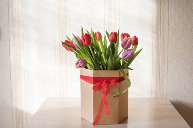 Güneşli bir günde, bir vazoda kırmızı ve mor laleler. Sevilen birinin hediyesi olan kurdeleli bir vazo.