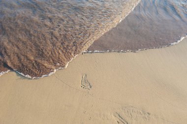 Sörf, batan güneşin altında kumların üzerinde denizden gelen bebek ayak izlerini örter.