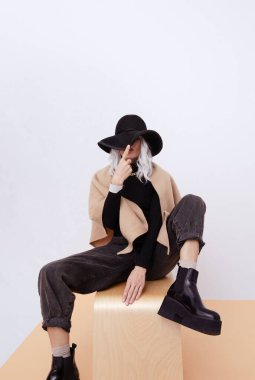Stüdyodaki kadın sıradan bir sonbahar kış kıyafeti giyiyor. Moda minimalist aşığı. Günlük bakışın ayrıntıları. Moda aksesuar şapka, atkı ve şık platform çizmeleri