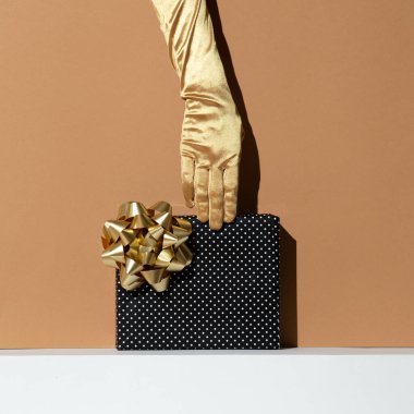 Elinde hediye kutusu olan altın eldivenleri teslim et. Asgari yaşam tasarımı. Tatil, Noel, doğum günü konsepti. Şimdiki fikir