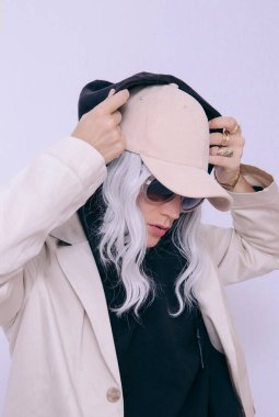 Beyaz stüdyodaki sarışın manken. Siyah kapüşonlu, modaya uygun bej kıyafetler. Kaptan, Denim Takım Ceket ve Pantolon. Sokak stili. Sonbahar mevsimi. Moda arama kitabı konsepti