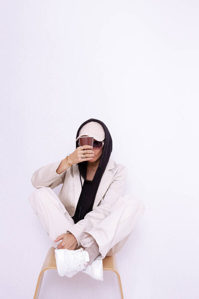 Model in white studio. Trendy beige casual outfit with black hoodie accent.  Cap, sunglasses, Denim Suit Jacket and Pants. Street Urban Style. Fall winter season.  Fashion lookbook concept. Coffee time