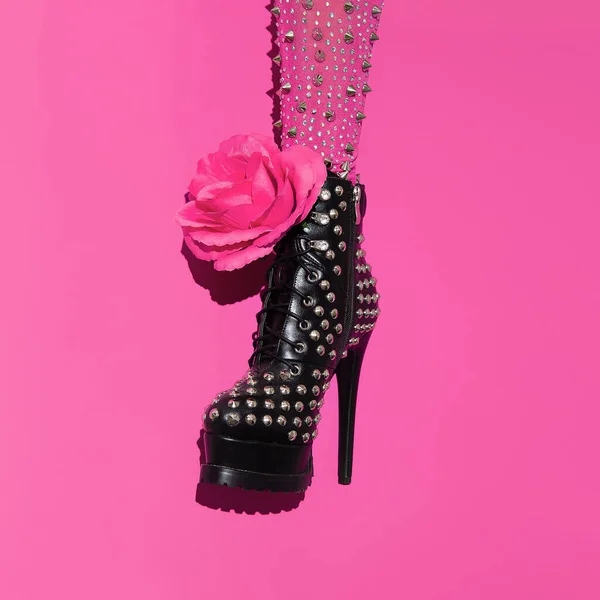 Fashion leg in heel black boots and pink roses on minimal pink background. Stylish accessories shoes concept