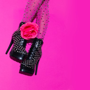 Moda bacakları ve topuklu güller. Pembe arka planda siyah çizmeler. Şık aksesuar ayakkabı konsepti