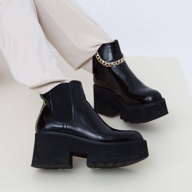 Sonbahar kıyafetlerinin modaya uygun ayrıntıları. Stüdyoda bej pantolon giyen ve zincirli siyah çizmeli bir kadın. Her gün bak. Sokak modası konsepti. Yüzü yok.