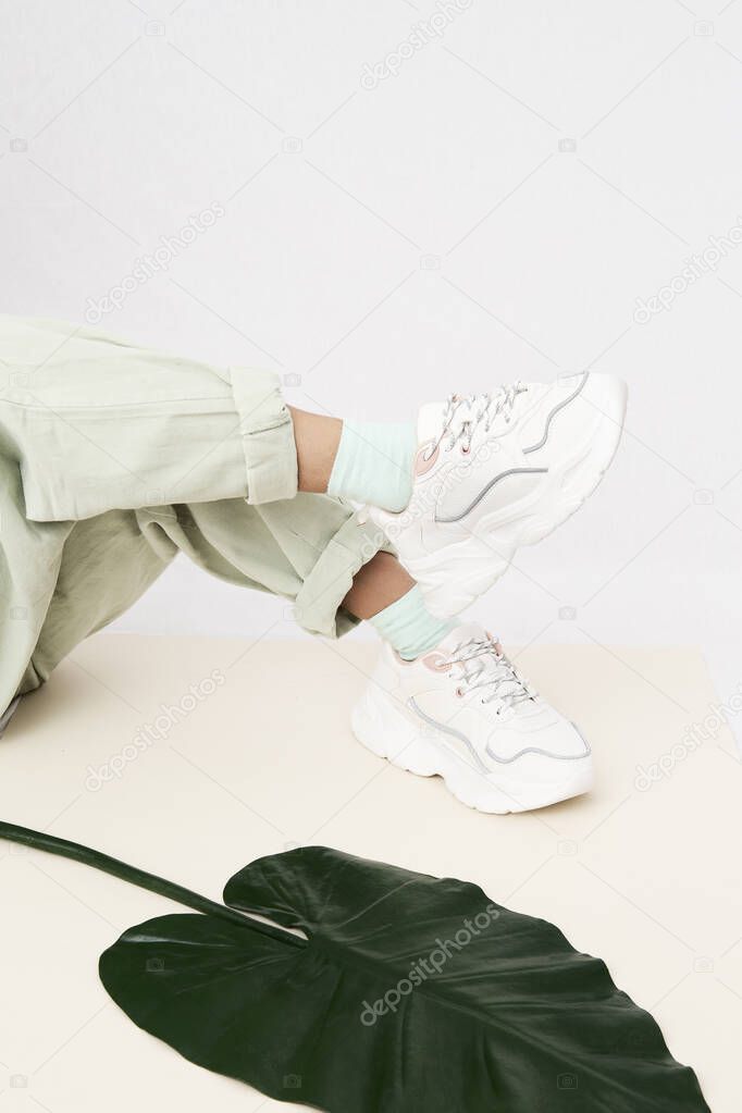 Details of trendy casual spring summer fresh outfit. Girl in studio wearing khaki jeans and stylish white sneakers. Everyday look. No face. Minimalist ecological vegan friendly clothing concept