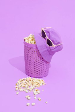 Mor patlamış mısır kovası ve güneş gözlüklü şapka. Hala hayat tasarımı. Moda ev sinema konsepti