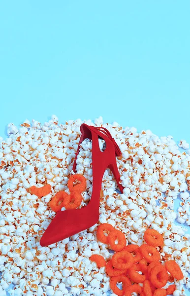 Minimal popcorn, corn rings background and fashion lady red shoes. Still life vertical design.  Diet, fast food, calory, unhealthy food concept.