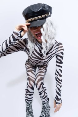 Çılgın zebra desenli kıyafetleri ve beyaz bir stüdyoda poz veren siyah deri şapkalı seksi androjenik sarışın manken. Kulüp parti tarzı