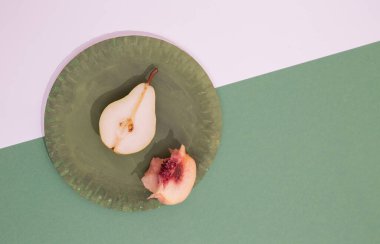 Taze minimalist sahne. Yeşil tabakta organik armut ve şeftali ve iki renkli kağıt arka plan. Sıfır atık, biyoloji, çevre, vegan konsept. Gösterişli düz pankart