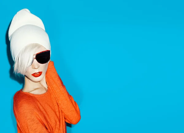 Moda menina loira com boné na moda e óculos de sol em uma parte traseira azul — Fotografia de Stock