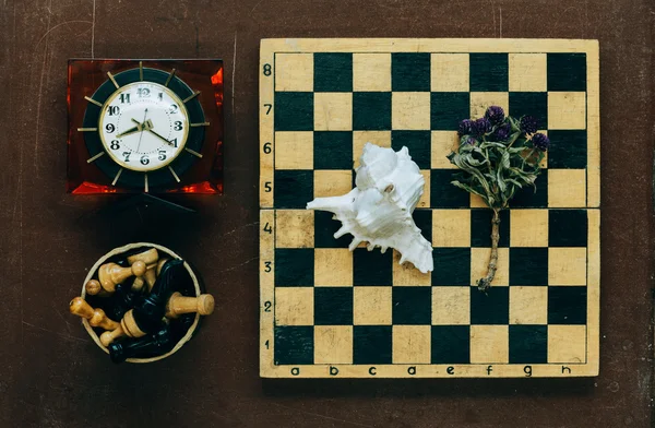 Chess, clock and seashell on old wooden background — Stock Photo, Image