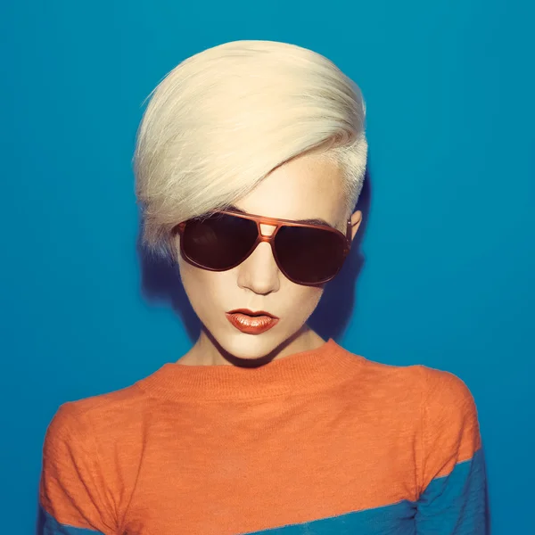 Blonde with fashionable hairstyle and sunglasses on a blue backg — Stock Photo, Image