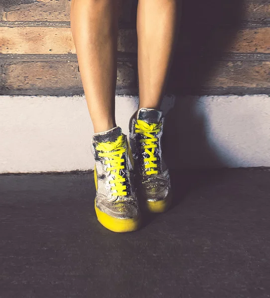 Ragazza in piedi in scarpe da ginnastica alla moda muro di mattoni. Moda urbana — Foto Stock