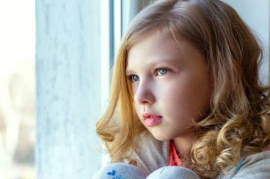 Güzel kız pencere eşiğinde oturuyor ve pencereden dışarı bakıyor.