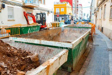 İspanya, Valencia, 29 Mart 2024: Toprak ve moloz dolu konteynırlar hareketli bir şehir caddesinde duruyor ve devam eden inşaat çalışmalarını gösteriyor.