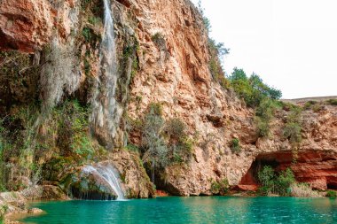 Göz kamaştırıcı bir şelale, canlı bitki ve ağaçlarla çevrili yüksek uçurumlardan akar ve sakin bir doğal ortam yaratır..