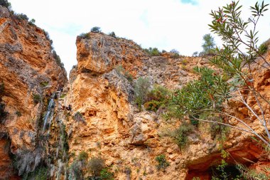 Parlak turuncu kil duvar, güneş ışığıyla aydınlatılan küçük çakıl taşları ve doğal dokulardan oluşan bir dizi sergiler..