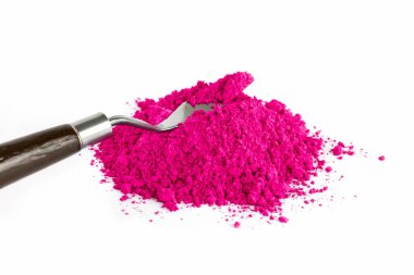 A vibrant magenta powder sits in a pile beside a gardening tool on a clean white surface, highlighting the rich color and texture.