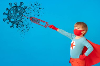 İçeride koruyucu maske takan süper kahraman çocuk. Süper kahraman çocuğun portresi mavi kağıttan arka planda. Aşı kavramı