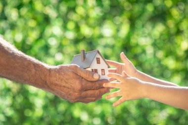 Baharın yeşil arka planına karşı aile çevre evini elinde tutuyor. Gayrimenkul ve Dünya Günü konsepti