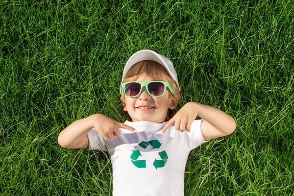 아동복은 티셔츠에 재활용 표지판을 손가락으로 가리킨다 배경에 대항하는 재밌는아이 생태학 — 스톡 사진