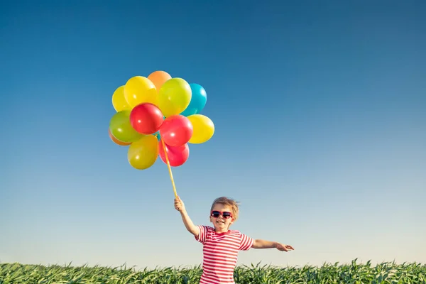 明るい多色の風船を屋外で遊んで幸せな子供 青い空を背景に緑の春のフィールドで楽しんでいる子供 健康で活動的なライフスタイルのコンセプト — ストック写真