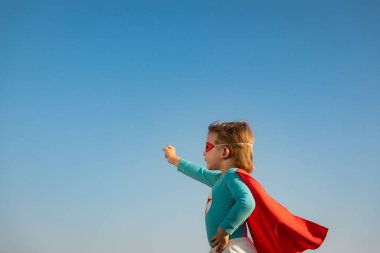 Mavi yaz gökyüzü arka planına karşı süper kahraman çocuk. Süper kahraman çocuk dışarıda eğleniyor. Özgürlük ve hayal gücü kavramı