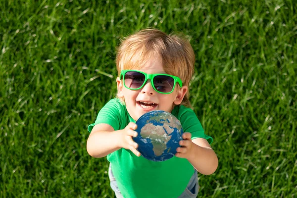 Child holding 3D planet in hands against green blurred background. Earth day spring holiday concept. Elements of this image furnished by NASA. Top view