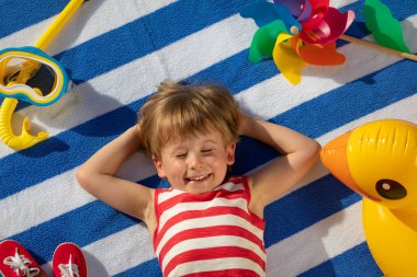 Dışarıda çizgili havlunun üzerinde yatan mutlu çocuk. Çocuk portresi. Gülen komik bebek. Yaz tatili kavramı