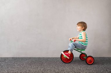 Fotokopi alanı olan gri beton arka planda klasik trike kullanan mutlu çocuk. Yeşil bahar konsepti