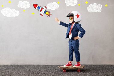 Gri beton arka planda kaykaya binen takım elbiseli mutlu çocuk. Çocukluk hayalleri ve iş fikri