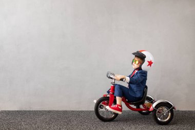 Gri beton arka planda bisiklet süren takım elbiseli mutlu çocuk. Çocukluk hayalleri ve iş fikri