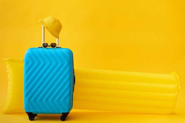 Blue suitcase against yellow background. Summer vacation and travel concept