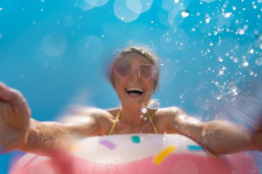 Happy woman having fun on summer vacation outdoor. Girl jumping in water against blue sky. Motion blur
