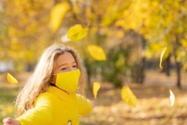 Dışarıda koruyucu maske takan mutlu bir çocuk. Sonbahar parkında eğlenen bir kız. Özgürlük ve salgın koronavirüs COVID 19 konsepti