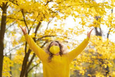 Dışarıda koruyucu maske takan mutlu bir çocuk. Sonbahar parkında eğlenen bir kız. Özgürlük ve salgın koronavirüs COVID 19 konsepti