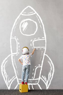 Büyük düşün! Mutlu çocuk dışarıda oynuyor. Komik çocuk duvara tebeşir roketi çiziyor. Uzay hakkında rüya gören çocuk. Çocuk astronot gibi davranıyor. Çocuklar hayal ve hayal gücü konsepti 