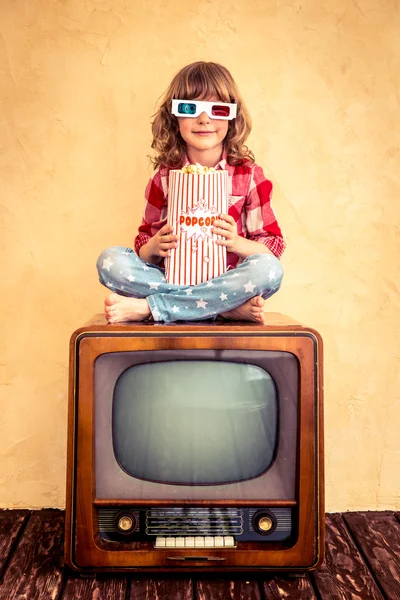 Kind sitzt auf Retro-Fernseher und isst Popcorn. — Stockfoto