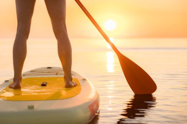 Genç bir kadın yaz tatilinde deniz kenarında ayağa kalkıp kürek çekiyor. Deniz ve gökyüzü arka planında kürek çeken güzel bir kız.